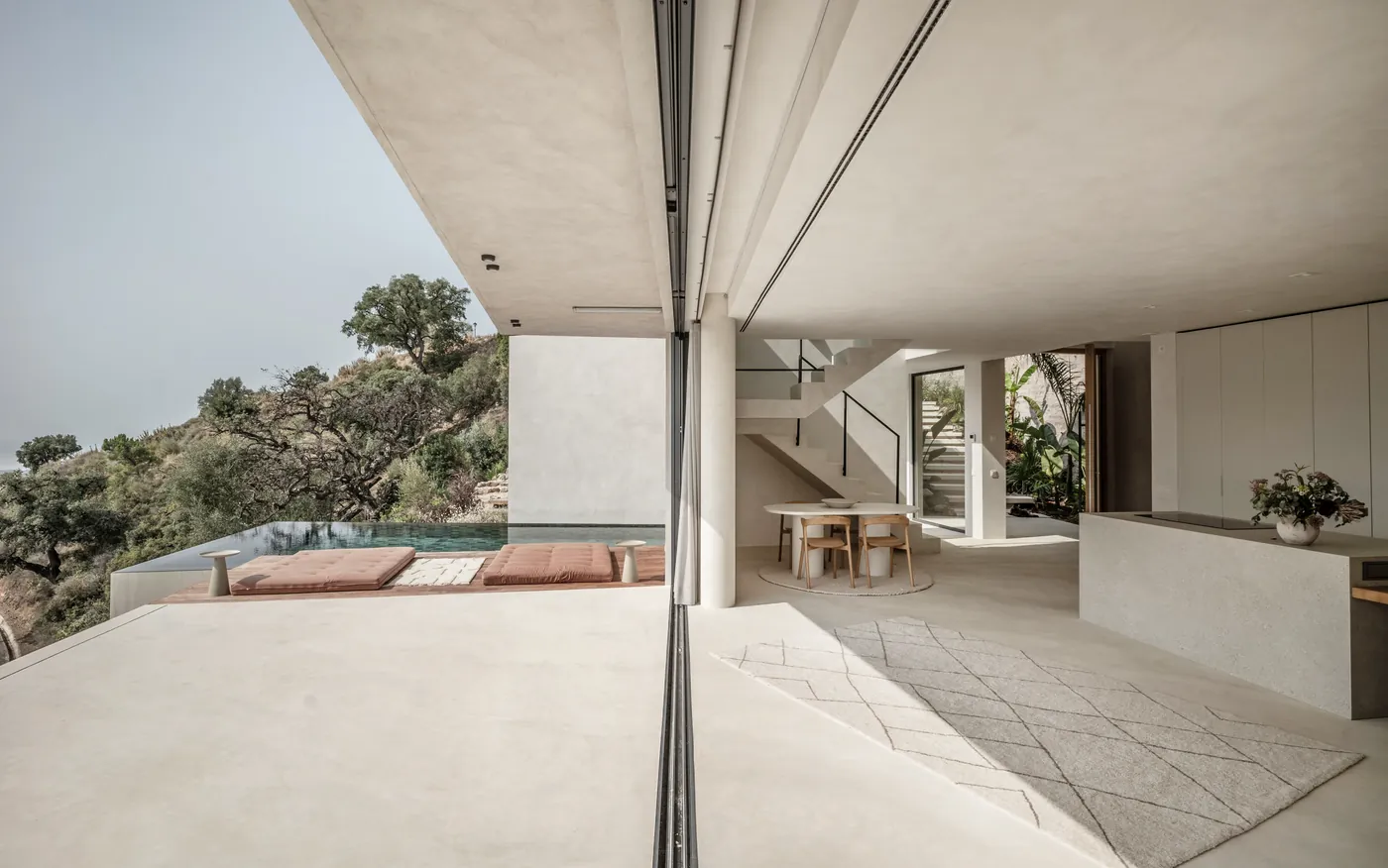 Die Glaswand ganz geöffnet zwischen Wohnbereich und Terrasse, dahinter der Pool