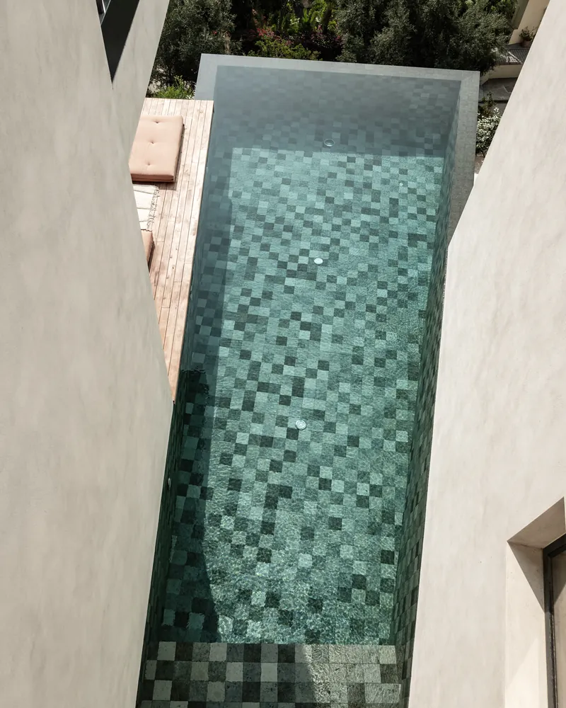 Der schmale Pool aus grünem Glasmosaik senkrecht von oben, zwischen weißen Mauern